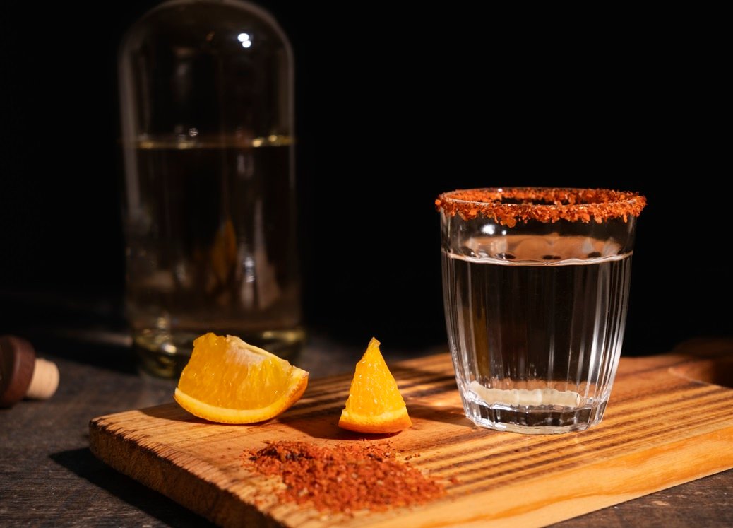 Mezcal jove-cristalino servido en vaso de veladora acompañado de naranjas